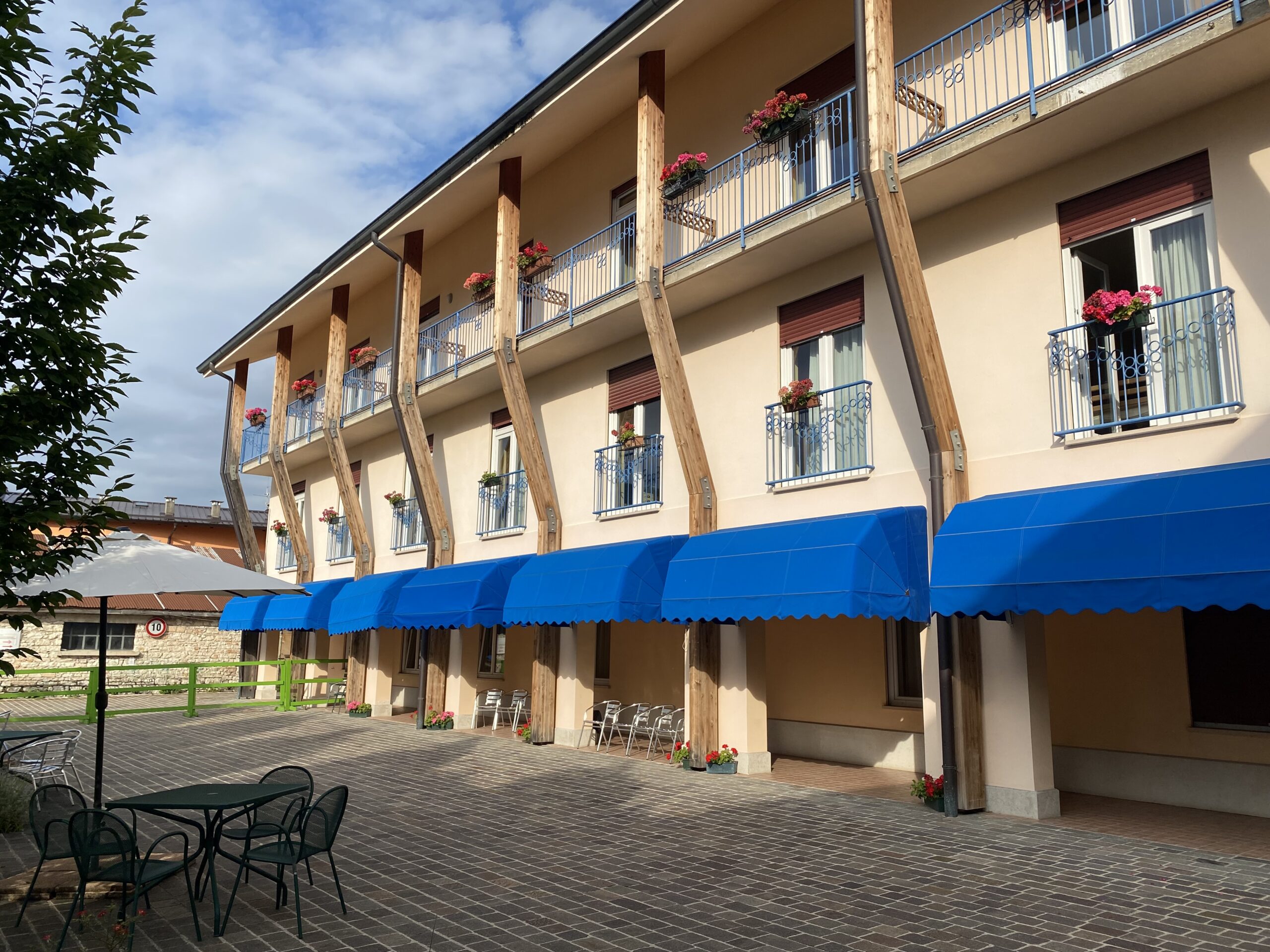 Edificio arancione chiaro a tre piani con spazio pavimentato di fronte. Le finestre del piano terra hanno tende a cappottina blu.